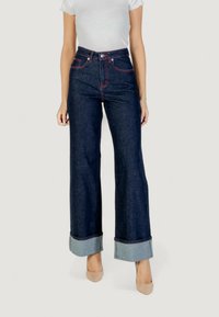 Jeans de mezclilla oscuros de tiro alto y pernera acampanada con costuras rojas y dobladillos remangados. Presenta un diseño clásico de cinco bolsillos.
