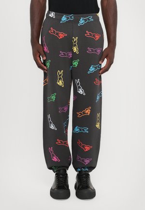 Black jogger pants featuring a multicolored cartoon rabbit pattern. Elastic waistband and cuffs. Worn with black sneakers.