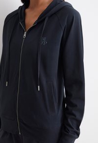 Felpa con zip color navy realizzata in materiale morbido, con cappuccio regolabile, due tasche frontali e un logo discreto sul petto.