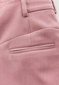 Pantaloni roz dintr-un material texturat, cu un buzunar plat și aerodinamic în spate și cusături croite. O strălucire subtilă îmbunătățește aspectul general.