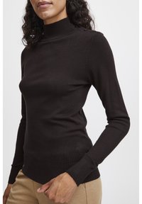 Brun stickad turtleneck tröja med en figurnära design, ribbade mudd och nederkant, med knappar på vänster axel för extra detalj.