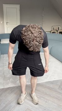 Calções de desporto pretos com um corte solto, apresentando bolsos laterais e um logótipo no lado inferior esquerdo, usados com ténis bege.