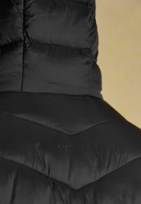 Čierna prešívaná bunda z pohľadu zozadu s vysokým golierom a diskrétnym embosovaným logom "Joules" na látke.