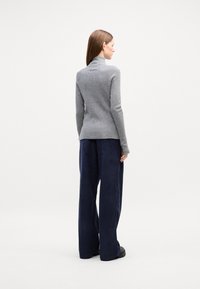 Grau gerippter Rollkragenpullover kombiniert mit navyblauen weiten Cordhosen. Das Outfit hat lange Ärmel und eine figurbetonte Silhouette.