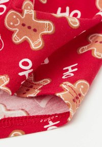 Czerwona tkanina z wzorem piernikowego ludzika w kolorach beżowym i białym, cechująca się miękką fakturą i wykończeniem z podwiniętym brzegiem.