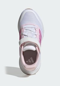Zapato deportivo blanco con detalles rosa, parte superior de malla transpirable, diseño con cordones y una correa de velcro. Suela exterior redondeada de goma.