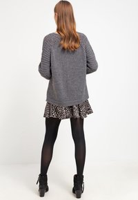Gray knitted sweater with textured sleeves, paired with a black patterned skirt. The person wears black tights and ankle boots.