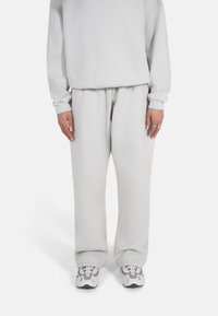 Lys grå hettegenser og matchende joggebukser laget av mykt stoff. Løs passform med ribbede mansjetter. Brukt med grå og hvite joggesko.