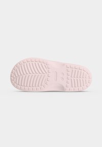 Semelle de chaussure en caoutchouc rose clair avec des motifs de bande de roulement texturés et le logo Crocs au centre sur un fond clair uni.