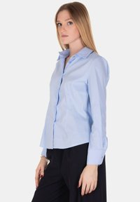 Camicia button-up azzurra in cotone con maniche lunghe, colletto a punta e design aderente. Presenta una leggera trama e spacchi laterali.