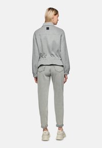 Graue Fleecejacke mit Kragen und elastischem Bund, kombiniert mit grauen Hosen mit aufgekrempelten Säumen. Minimalistisches Design mit dezenter Textur.