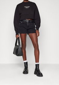 Svart cropped sweatshirt med vit logga, parat med svarta denimshorts med fransade kanter. Avslutat med svarta ankelskor och en svart väska.