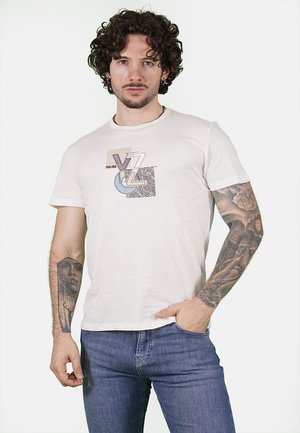 T-shirt di cotone color crema con design grafico che presenta il testo "YES ZEE" e motivi astratti. Maniche corte e collo a giro.