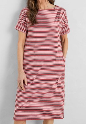 Woman wearing a knee-length, short-sleeve dress with horizontal pink and red stripes, standing with one hand in pocket.