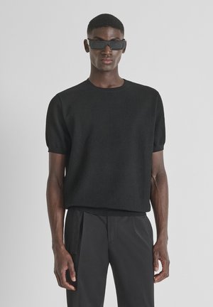 Suéter corto de punto acanalado negro de manga corta con un cuello redondo, combinado con pantalones negros elegantes, con un ajuste relajado y una textura sutil.