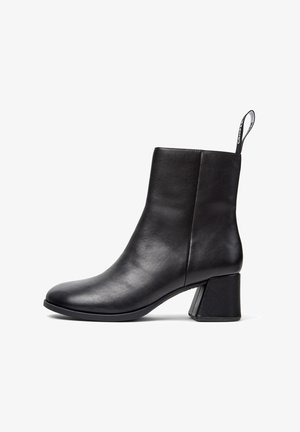 Svart läderankleboot med blockklack och dragflik, slät yta, sidovyu på vit bakgrund.