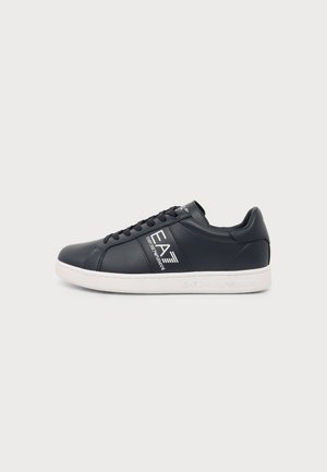 Zwarte lage sneaker met witte zool en EA7 Emporio Armani-logo aan de zijkant, veters zwart gesnoerd op een effen achtergrond.