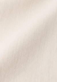 Vitt tyg med ett subtilt diagonalt vävmönster, som har en slät textur och en jämn färg över hela ytan.