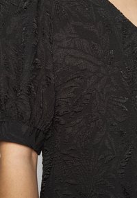 Mustan tekstuurin kangas, jossa on lehväkuvio, puffeilla hihoilla ja V-pääntie. Pehmeä, kevyt materiaali.