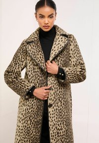 Płaszcz w panterkę z wyraźnym kołnierzem, długimi rękawami i czarnymi detalami przy mankietach i krawędziach. Miękka, teksturowana tkanina.