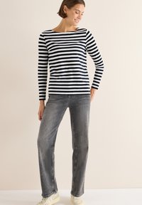 Broderet langærmet top i marineblå og hvid, parret med grå jeans. Teksturen virker blød; jeansene har en afslappet pasform og et falmet udseende.
