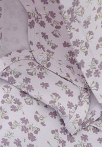 Lila blommönster på mjukt, ljust tyg med knäppningar. Har en delikat grön stilkar och gula inslag som framhäver det blommiga mönstret.