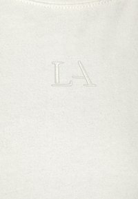 White cotton fabric with a smooth texture, featuring embossed letters "LA" in light color positioned centrally.