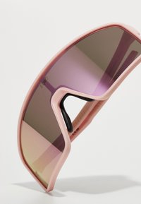 Ochelari de soare cu o ramă din plastic roz moale, lentile mari curbe cu un gradient de la violet la gri și un grip texturat pe brațe.