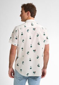 Camicetta bianca a maniche corte con tessuto texturizzato; presenta un motivo di piccole palme verdi e elementi rosa. Vestibilità casual e colletto a punta.