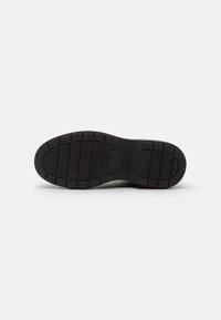 Svart skosula med en strukturerad design med ett rutmönster och en solid häl. Materialet verkar vara gummi utan synliga detaljer.