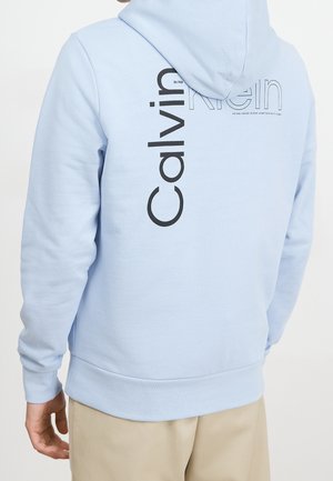 Lichtblauwe hoodie met een groot zwart "Calvin Klein" logo op de achterkant, voorzien van een trekkoord in de capuchon en geribde manchetten en zoom.