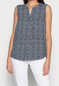 Top sans manches bleu marine avec un motif texturé blanc, un décolleté en V et une coupe décontractée, associé à un pantalon blanc.