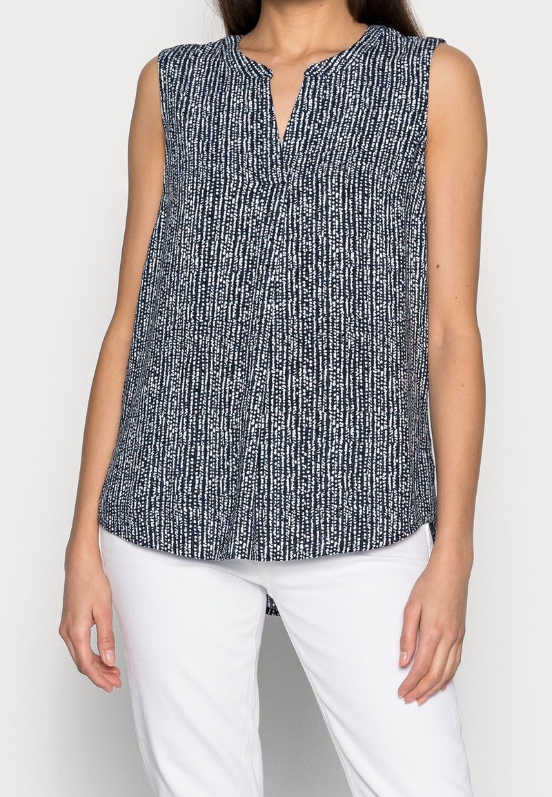 Top sans manches bleu marine avec un motif texturé blanc, un décolleté en V et une coupe décontractée, associé à un pantalon blanc.