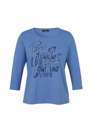 Blaues Langarmshirt mit rundem Ausschnitt und schwarzem handgeschriebenem französischem Text auf der Vorderseite mit dem Text "Paris est toujours une visite qui vaut la peine."
