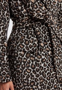 Lietussargs ar leopardu rakstu, mīksta auduma, ar savilktu jostas siksnu, sānu kabatu un krāsu paleti melnā, brūnā un krēmkrāsā.