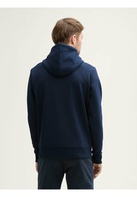 Sweatshirt à capuche bleu marine avec une finition texturée, manches longues et ourlet côtelé ; présente une coupe décontractée et un design minimaliste.