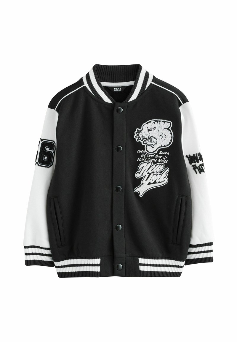 Giacca varsity nera con maniche bianche. Presenta una grafica di leone ricamata, accenti testuali e polsini e orlo a coste rigate. Chiusura frontale a scatti.