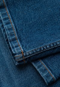 Tissu en denim de teinte bleu foncé, présentant une légère texture. Coutures orange distinctes le long des coutures, plié avec les bords visibles.