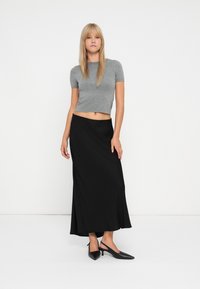 Un haut ajusté à manches courtes gris associé à une longue jupe noire ; le haut est côtelé et la jupe présente un design fluide. Des escarpins noirs à talons aiguilles complètent le look.