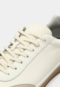 Witte leren sneaker met gestructureerde zijkanten, platte veters en een ronde neus. Bevat een rubberen zool en stiksel langs de zijkanten.