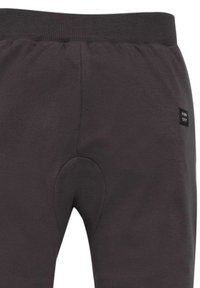 Dunkelgraue Jogginghosen verfügen über einen gerippten Bund, eine weiche Textur und ein dekoratives Nähmuster mit einem kleinen Logo-Patch an der Seite.