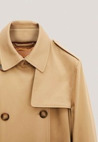 Beigefarbener Trenchcoat aus glattem Stoff mit einem doppelt knöpfbaren Design, großem Kragen und zwei braunen Knöpfen mit einer eleganten Textur.