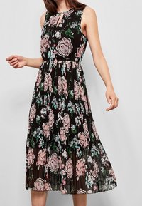 Blumen-Midi-Kleid mit schwarzem Hintergrund, das rosa und grüne Blumen zeigt. Ärmelloses Design, plissierter Stoff und Detail mit Schlüssel-ausschnitt im Dekolleté.
