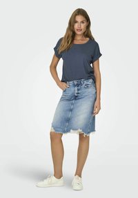 Jupe en denim à crayon avec un ourlet effiloché, couleur bleu clair ; associée à un haut à manches courtes bleu foncé et des baskets blanches, pour un style décontracté.