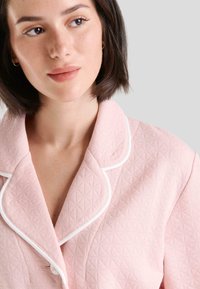 Pijama de color rosa claro con una textura de diamante, ribete blanco en el cuello y un diseño de solapa con muesca. Cierre de botones visible.