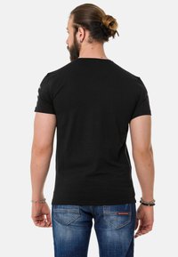 Schwarzes Kurzarm-T-Shirt mit rundem Halsausschnitt, aus Baumwolle. Kombiniert mit blauen Jeans im Denim-Stil, die einen ausgewaschenen Look und Gesäßtaschen haben.