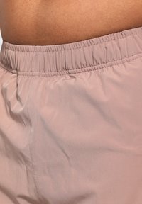 Ljusrosa elastisk midja med plisseringar, i kombination med ett mjukt, lätt tyg som övergår till mjuka draperingar. Inga synliga mönster eller detaljer.