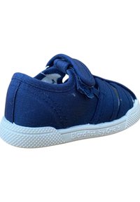 Zapato de lona navy con correa de velcro, suela de goma blanca y fondo texturizado. Presenta un diseño lateral con cortes y la marca "Blanditos by Crios".