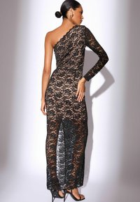 Mustaläbiga kleit eksitava disainiga; ühe pika varruka ja keha lähedase silueti ning läbipaistvate pitskihtide ja kõrge lõhenemisega.