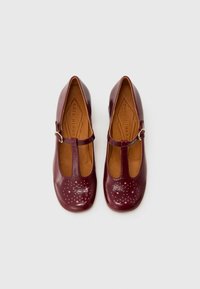 Scarpe in pelle borgogna con design a T, finitura lucida e punteggiatura decorativa rosa sulla punta. Suola piatta, forma della punta arrotondata.
